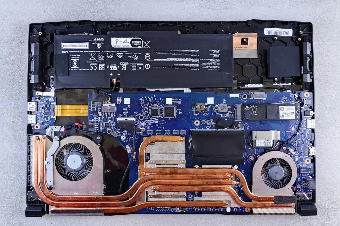 Notebook com a tampa inferior removida, mostrando placa-mãe, bateria, heatpipes e dois coolers