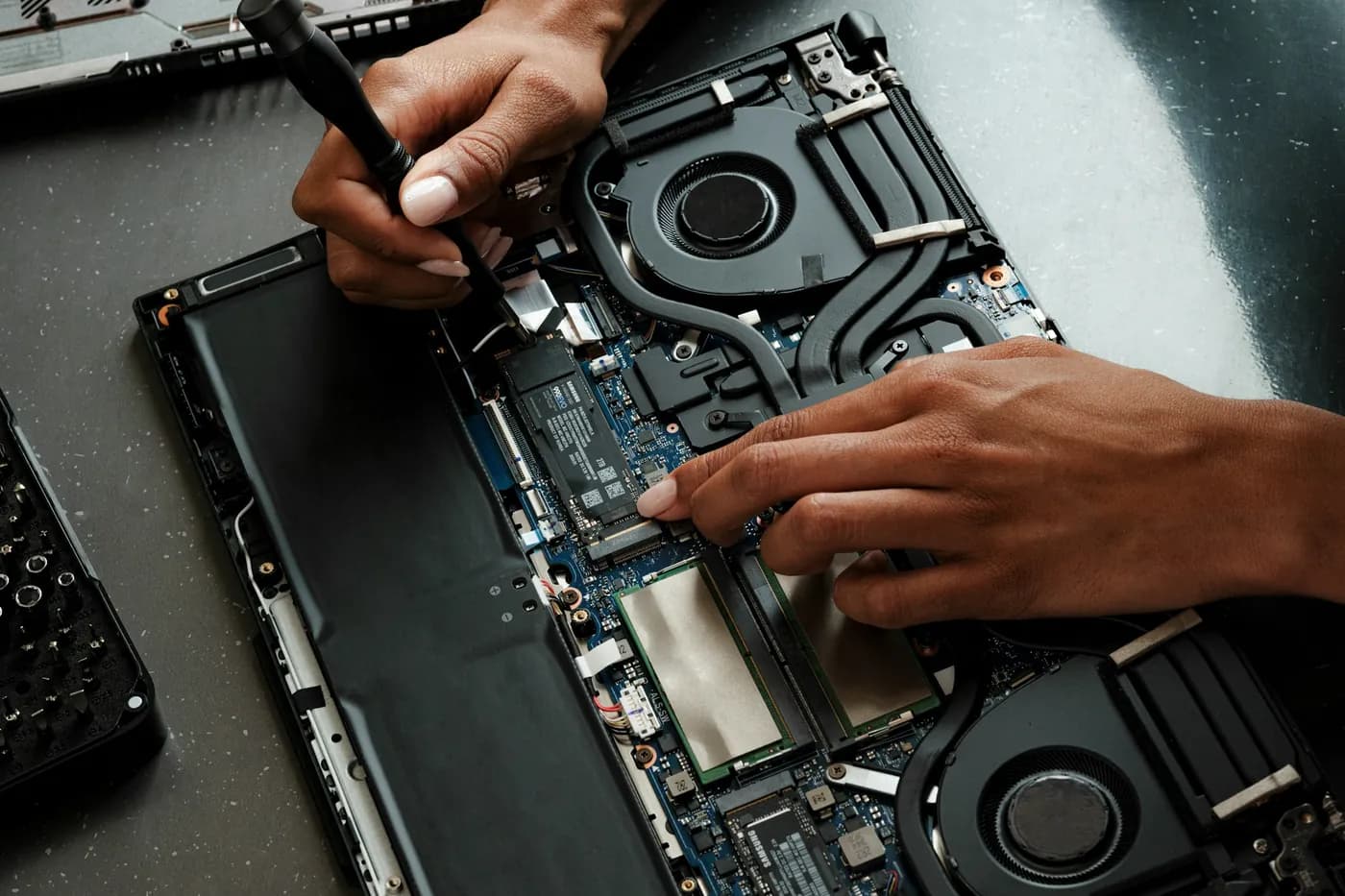 Mãos usando chave de fenda em um notebook aberto, com o SSD M.2 e os coolers à vista
